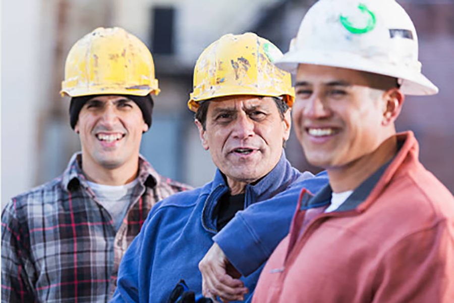 Three men wearing construction hats and smiling at the camera.